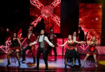 Best of Famous Musicals Sieben Darsteller:innen stehen in Rot-Schwarzen kostümen auf der Bühne und Singen